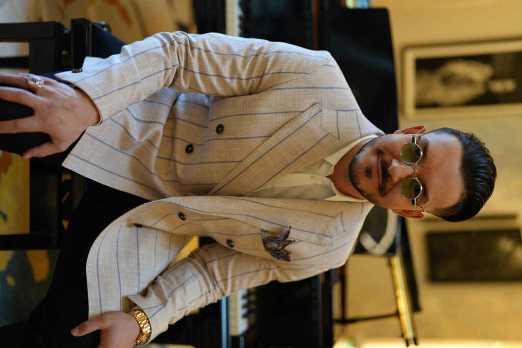 Maksim Asenov at a black grand piano in a cream pinstripe jacket
