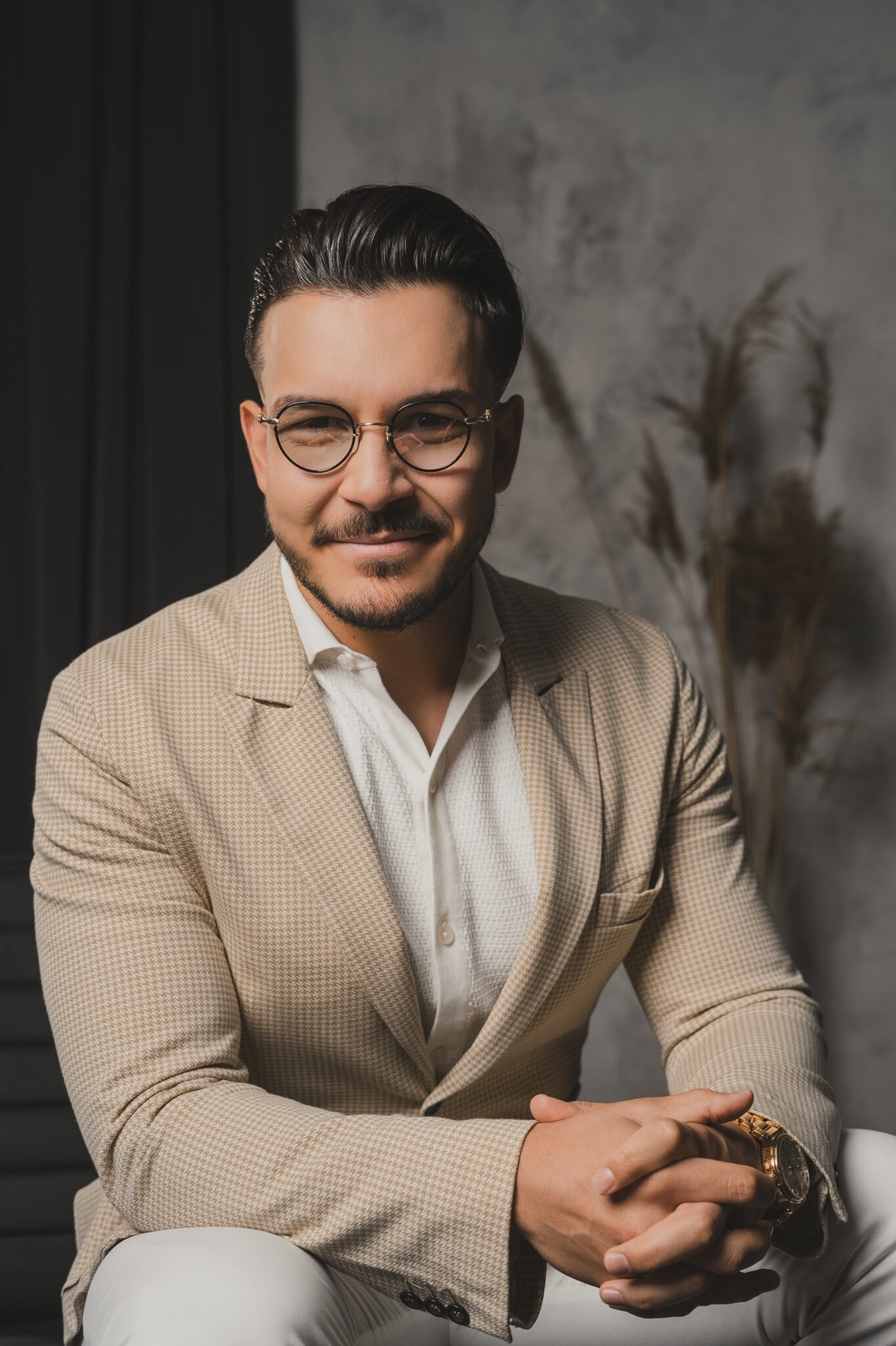 Maksim Asenov seated, leaning forward in a houndstooth blazer